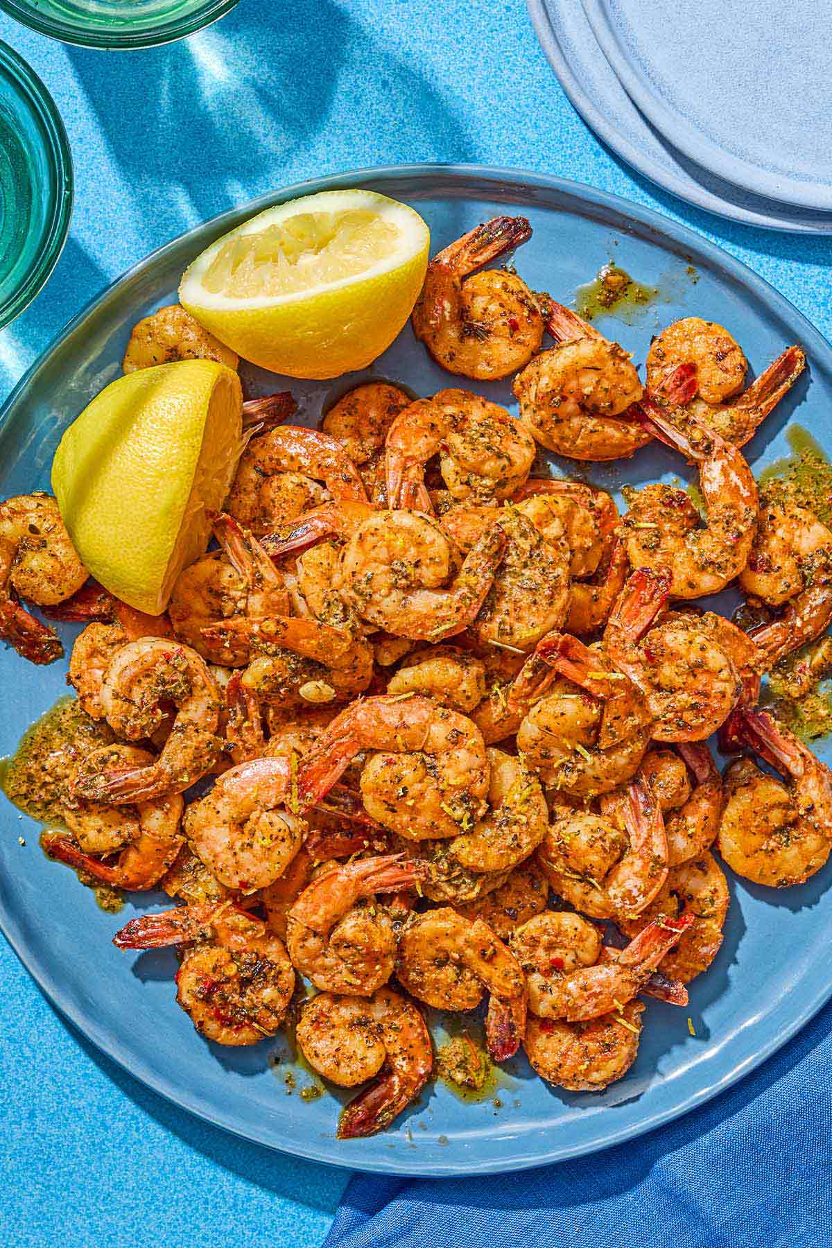 Sautéed shrimp with 2 juiced lemon halves on a platter. Next to this is a stack of 2 plates.