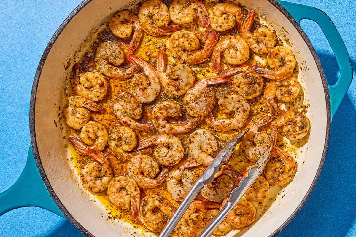 Sautéed shrimp in a skillet with a pair of tongs.