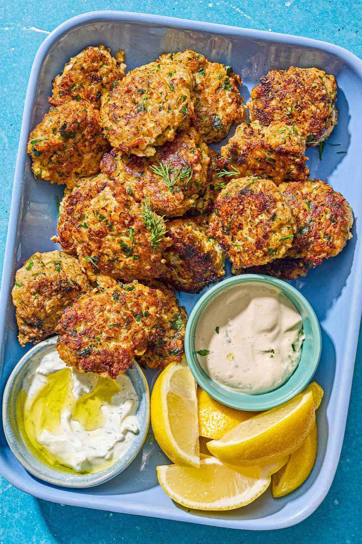 Shrimp kofta on a platter with bowls of tahini and tzaziki sauce and lemon wedges.