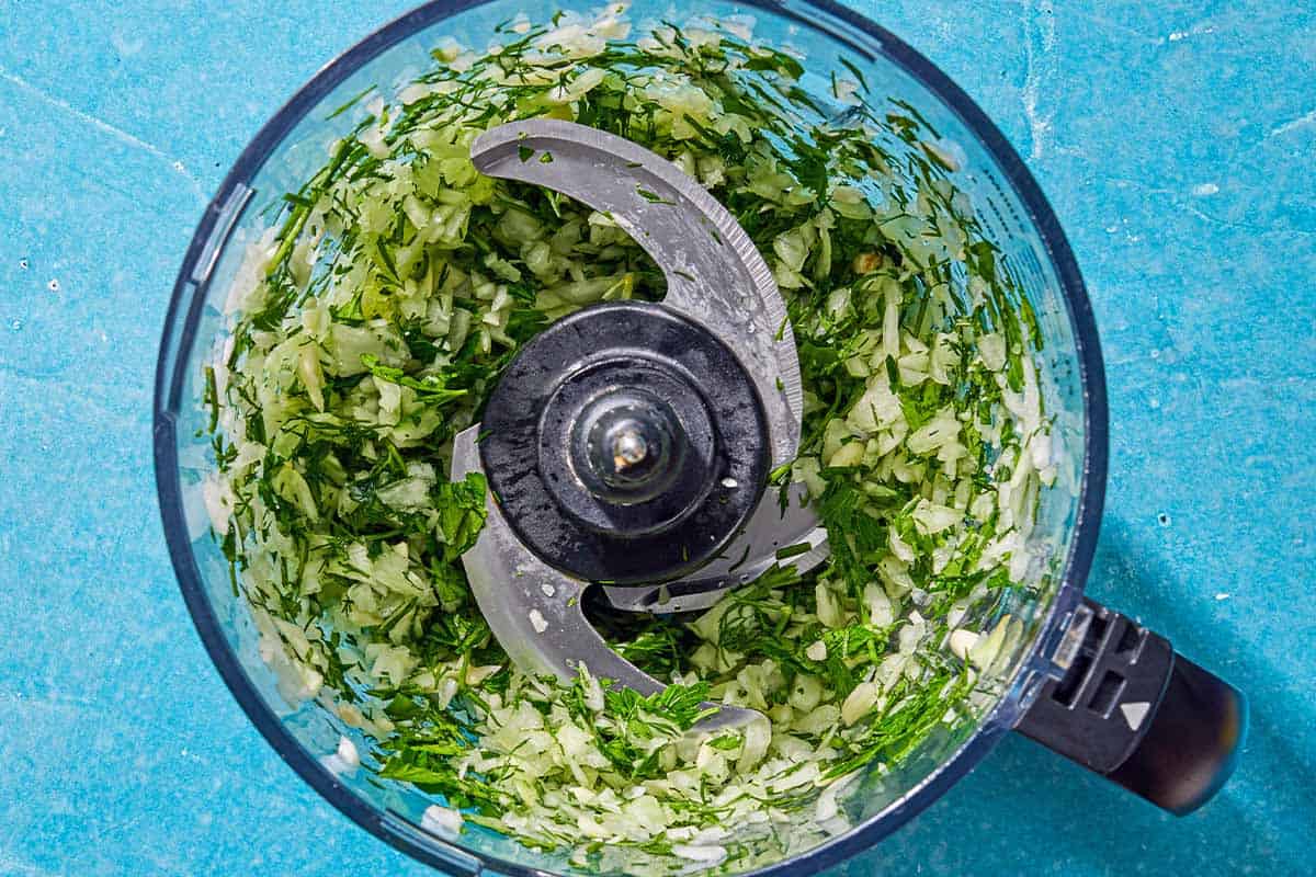 The onion, parsley, dill and garlic in the bowl of a food processor just after being mixed together.