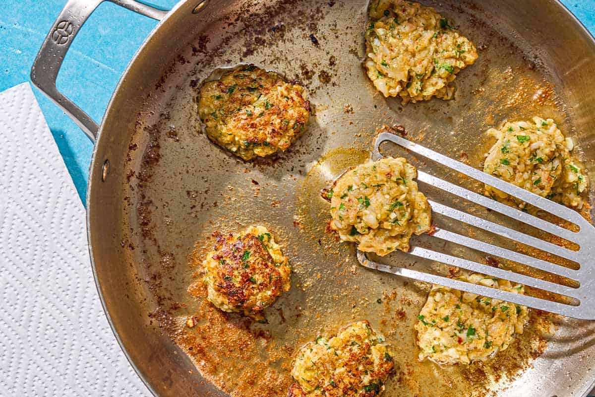 The shrimp kofta being fried in a skillet. One is in the process of being flipped over with a spatula.