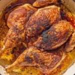 The whole cooked spatchcock chicken in a skillet.