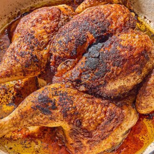 The whole cooked spatchcock chicken in a skillet.