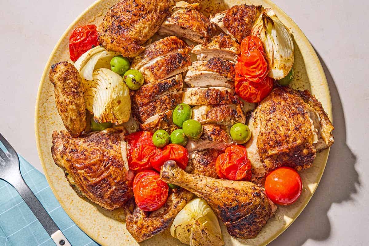 The spatchcock chicken pieces with olives, onion and tomatoes on a platter.