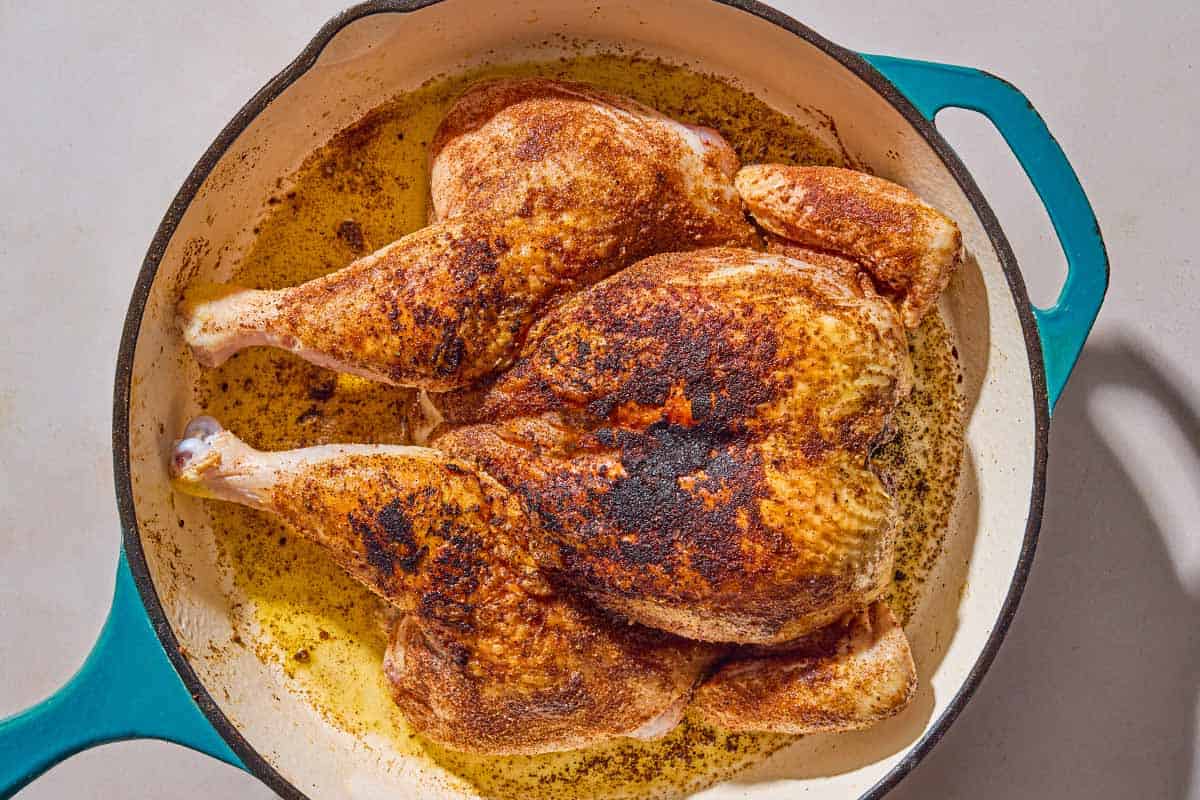 The whole cooked spatchcock chicken in a skillet.