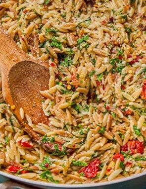 A close up of the orzo recipe in a skillet with a wooden spoon.