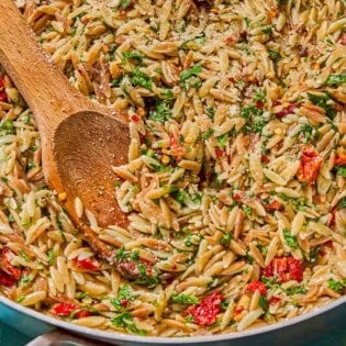 A close up of the orzo recipe in a skillet with a wooden spoon.