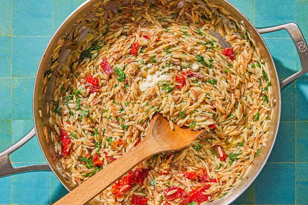 The orzo recipe being stirred in a skillet with a wooden spoon.