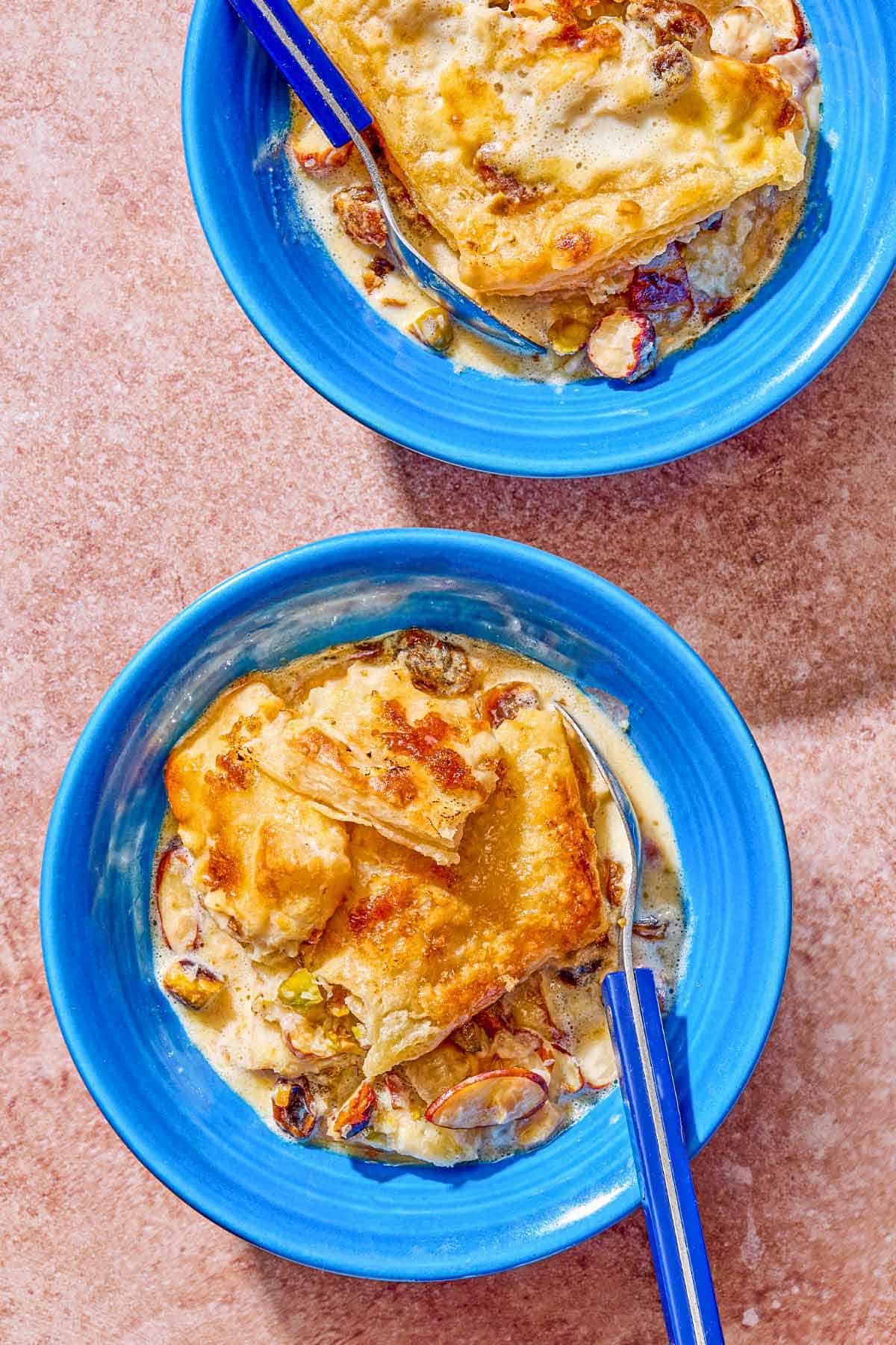 Two servings of bread pudding in bowls with spoons.