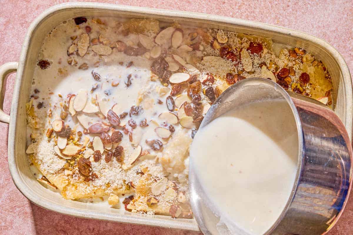 The milk mixture being poured over the unbaked bread pudding in the baking dish.