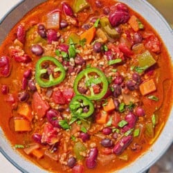 An overhead photos a bowl of vegan chili. Next to this is a glass of water, and a cloth napkin with a spoon.