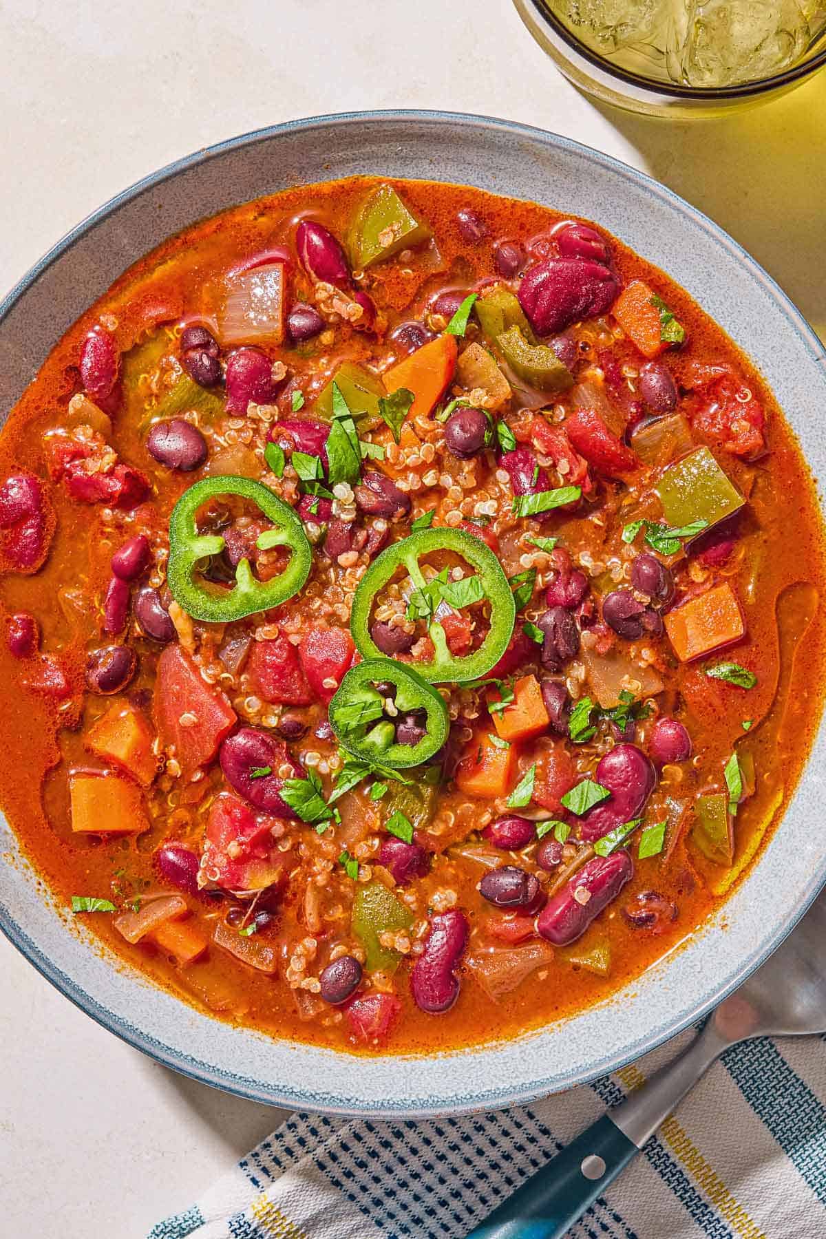 An overhead photos a bowl of vegan chili. Next to this is a glass of water, and a cloth napkin with a spoon.