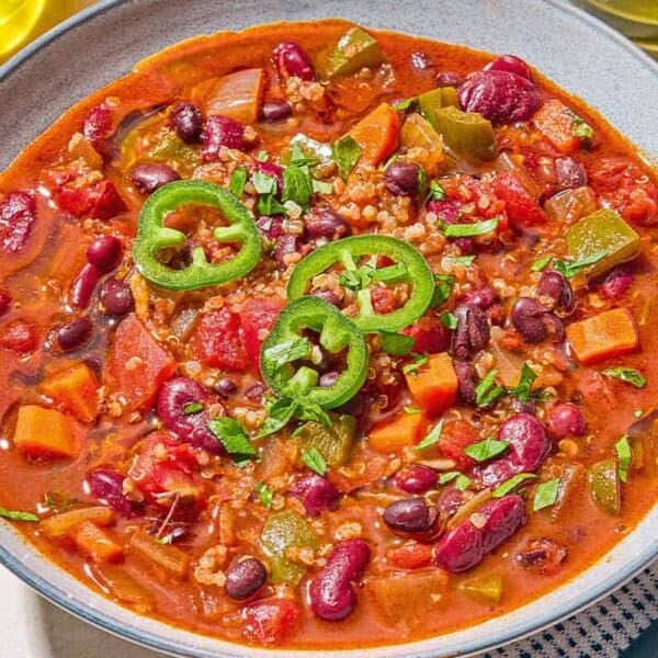 A bowl of vegan chili next to a cloth napkin with a spoon.