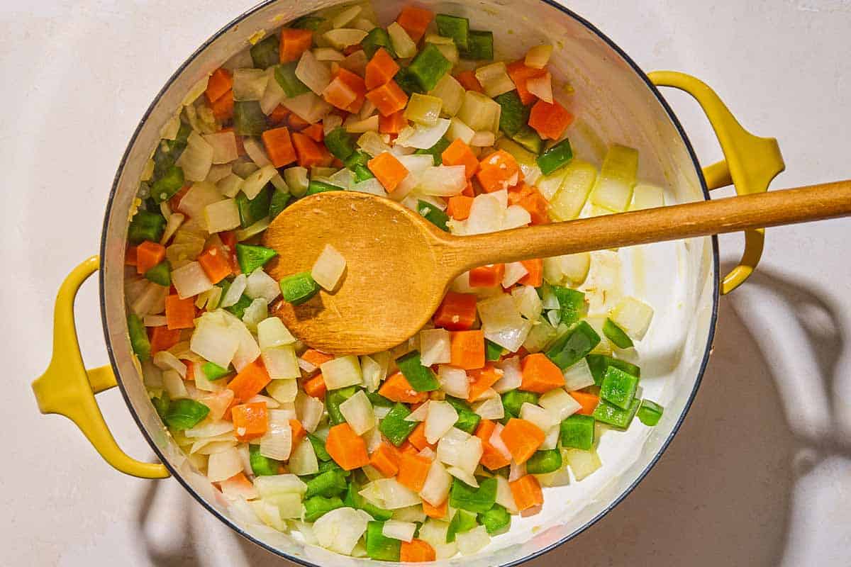 The chopped vegetables for the vegan chili being sauteed in a pot with a wooden spoon.