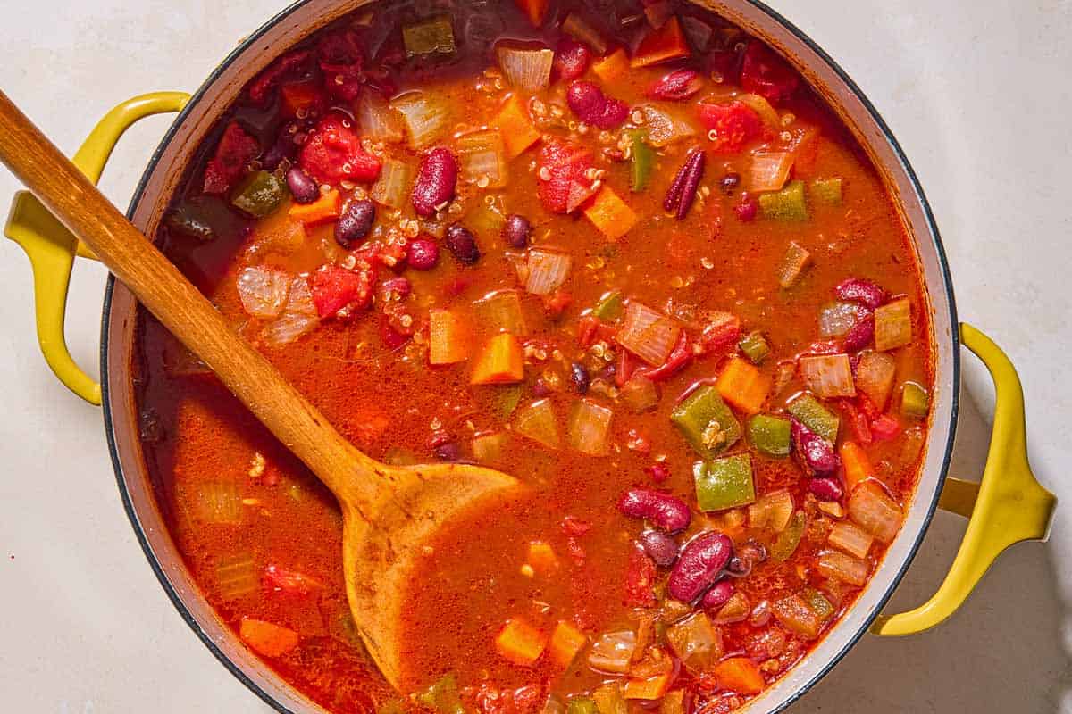 The vegan chili simmering in a pot with a wooden spoon.