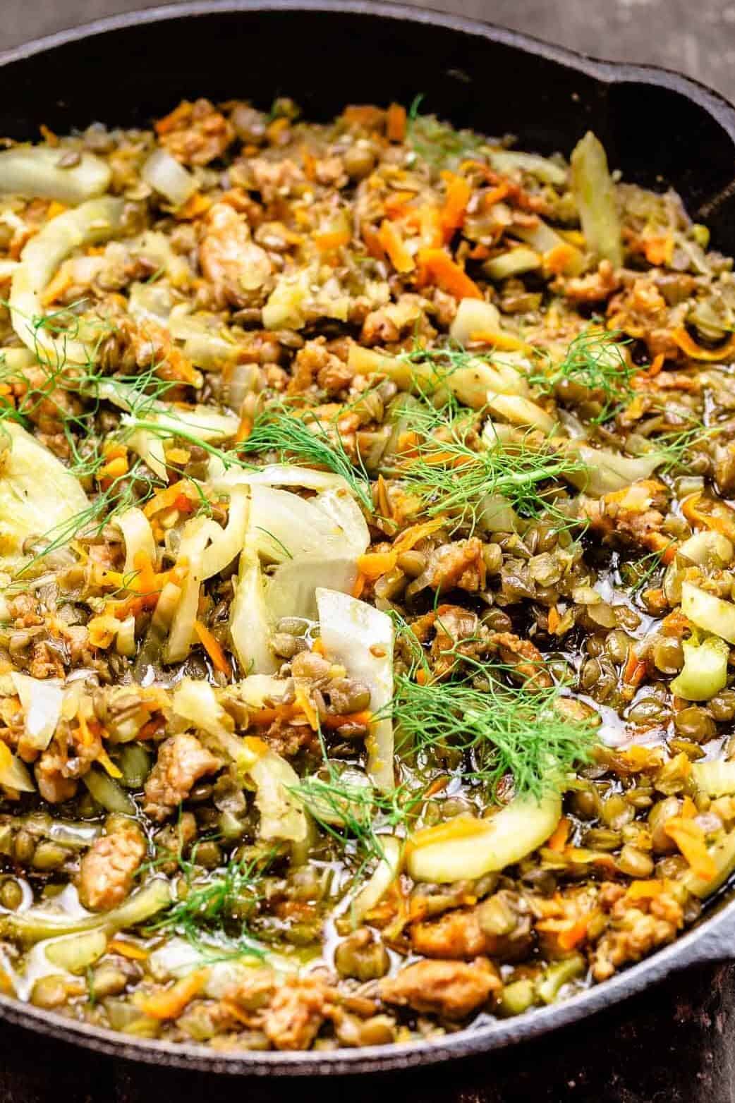 sausage and lentils in a skillet topped with fennel fronds.