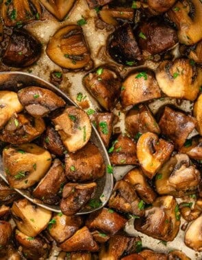 Spanish garlic mushrooms topped with chopped parsley in a saucepan with a spoon.
