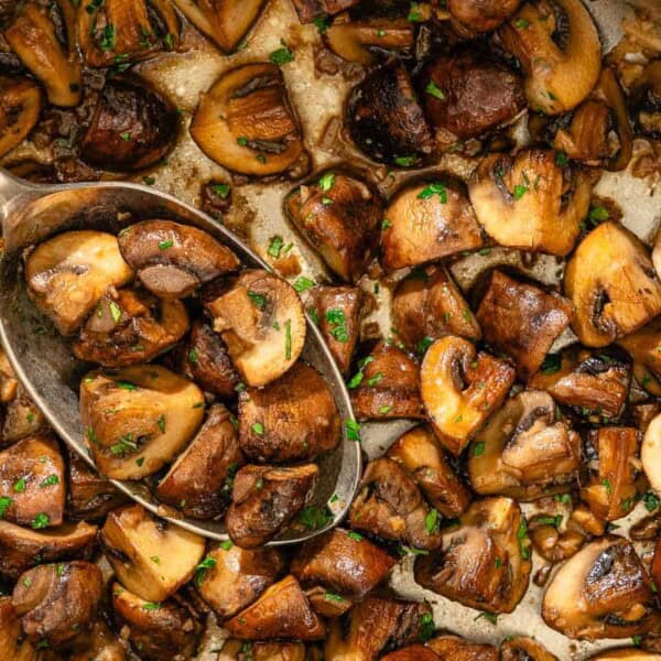 Spanish garlic mushrooms topped with chopped parsley in a saucepan with a spoon.