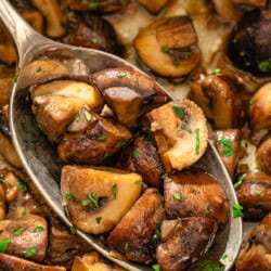 Spanish garlic mushrooms in a serving spoon being held over a bowl with the rest of the mushrooms.