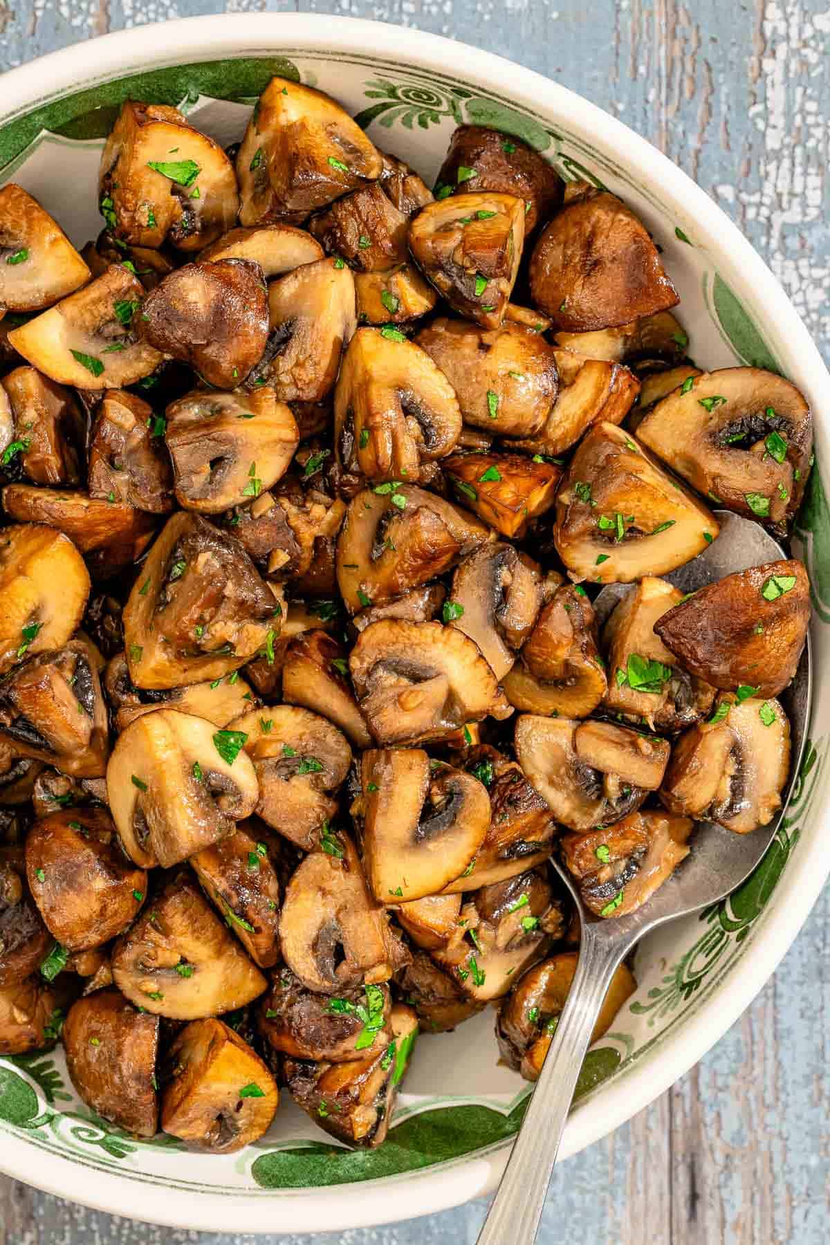 Spanish garlic mushrooms topped with chopped parsley in a serving bowl with a spoon.