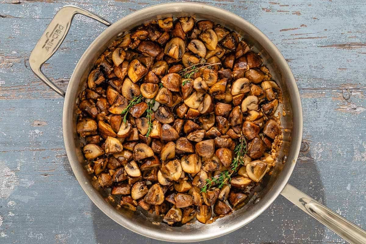 Spanish garlic mushrooms topped with fresh thyme in a saucepan.