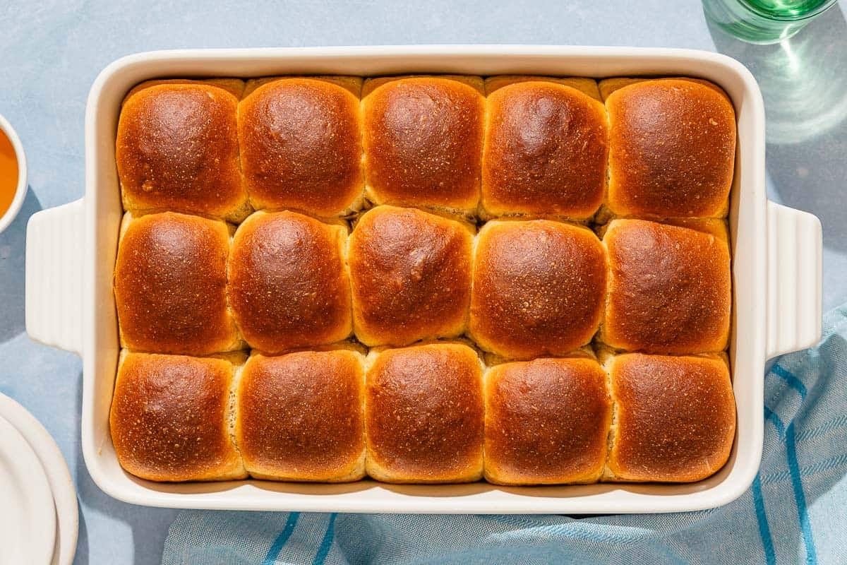 Baked dinner rolls in a baking dish next to a kitchen towel.