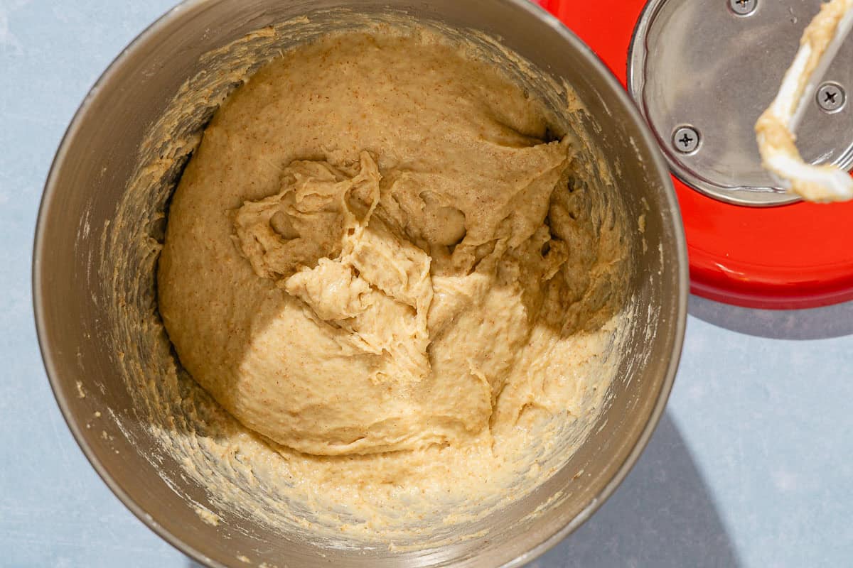 The dough for the dinner rolls in the bowl of a stand mixer. Next to this is the stand mixer.