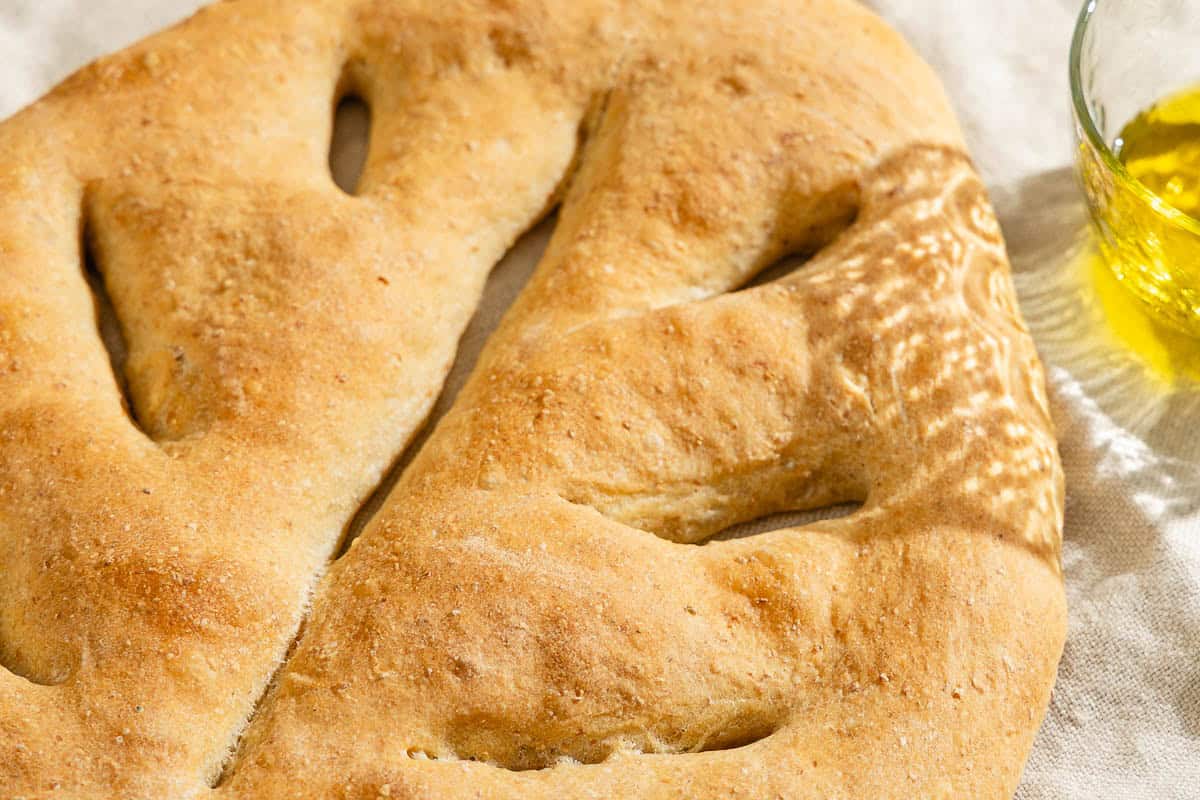 A close up of baked fougasse on a kitchen towel next to a small bowl of olive oil.