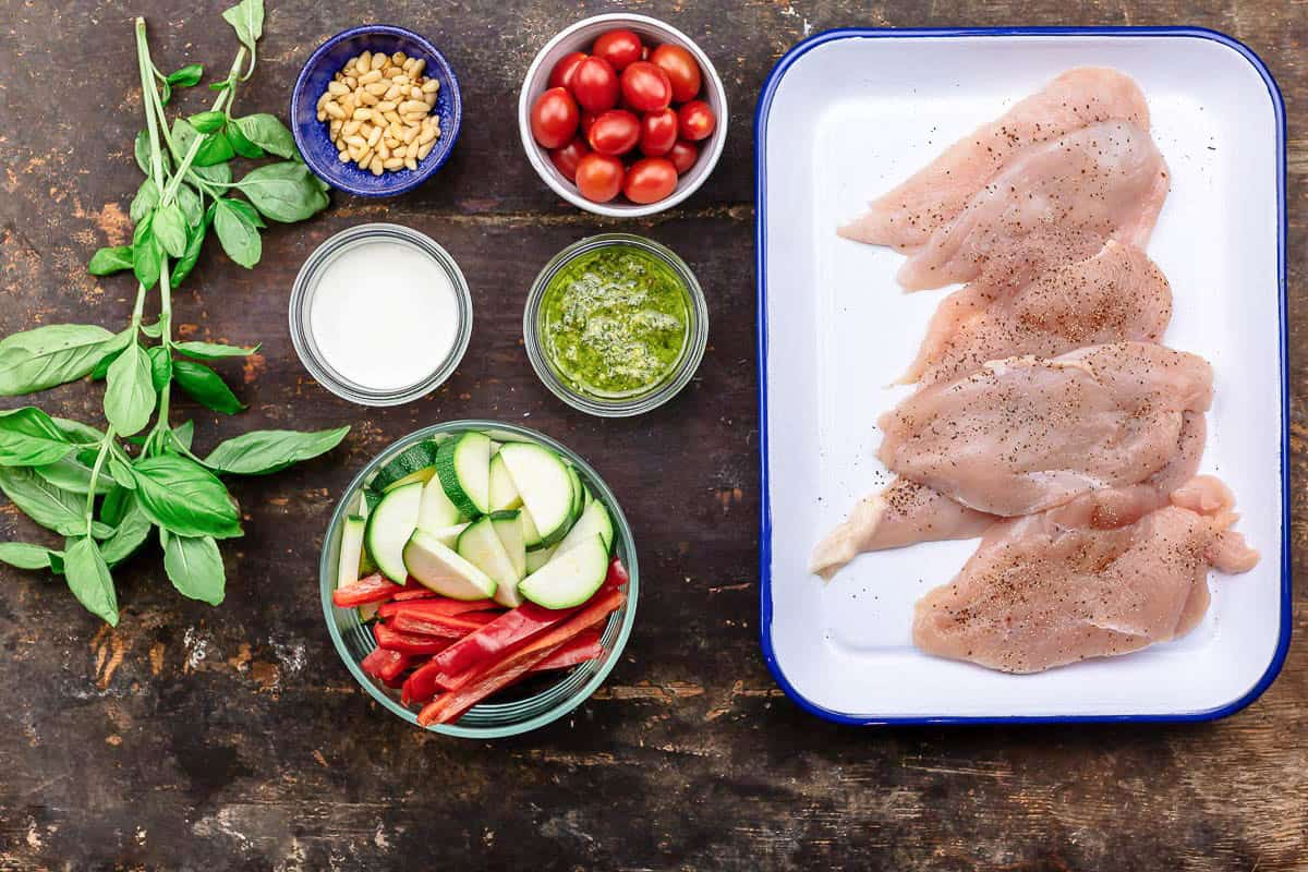 Ingredients for the chicken pesto chicken recipe including chicken cutlets, vegetables, cherry tomatoes, pesto, cream, basil and pine nuts.