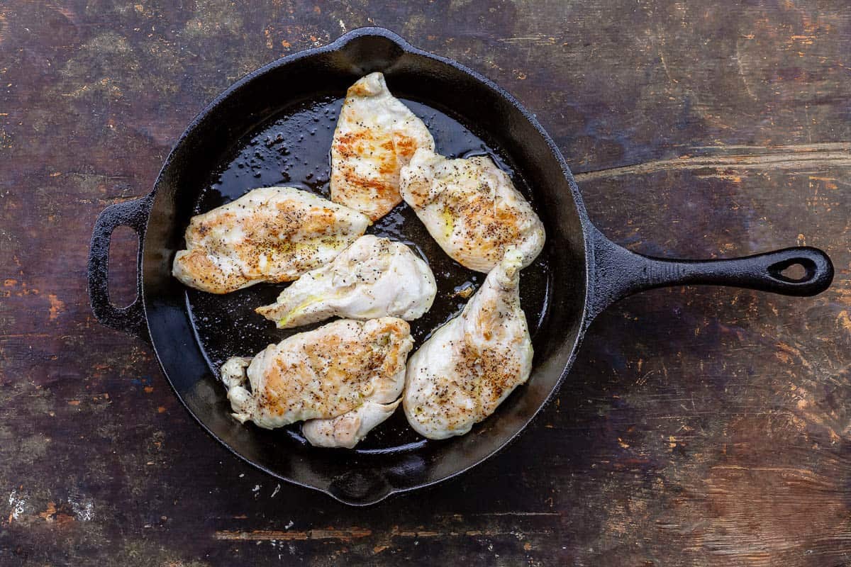 Cooked chicken cutlets for the pesto chicken in a cast iron skillet.