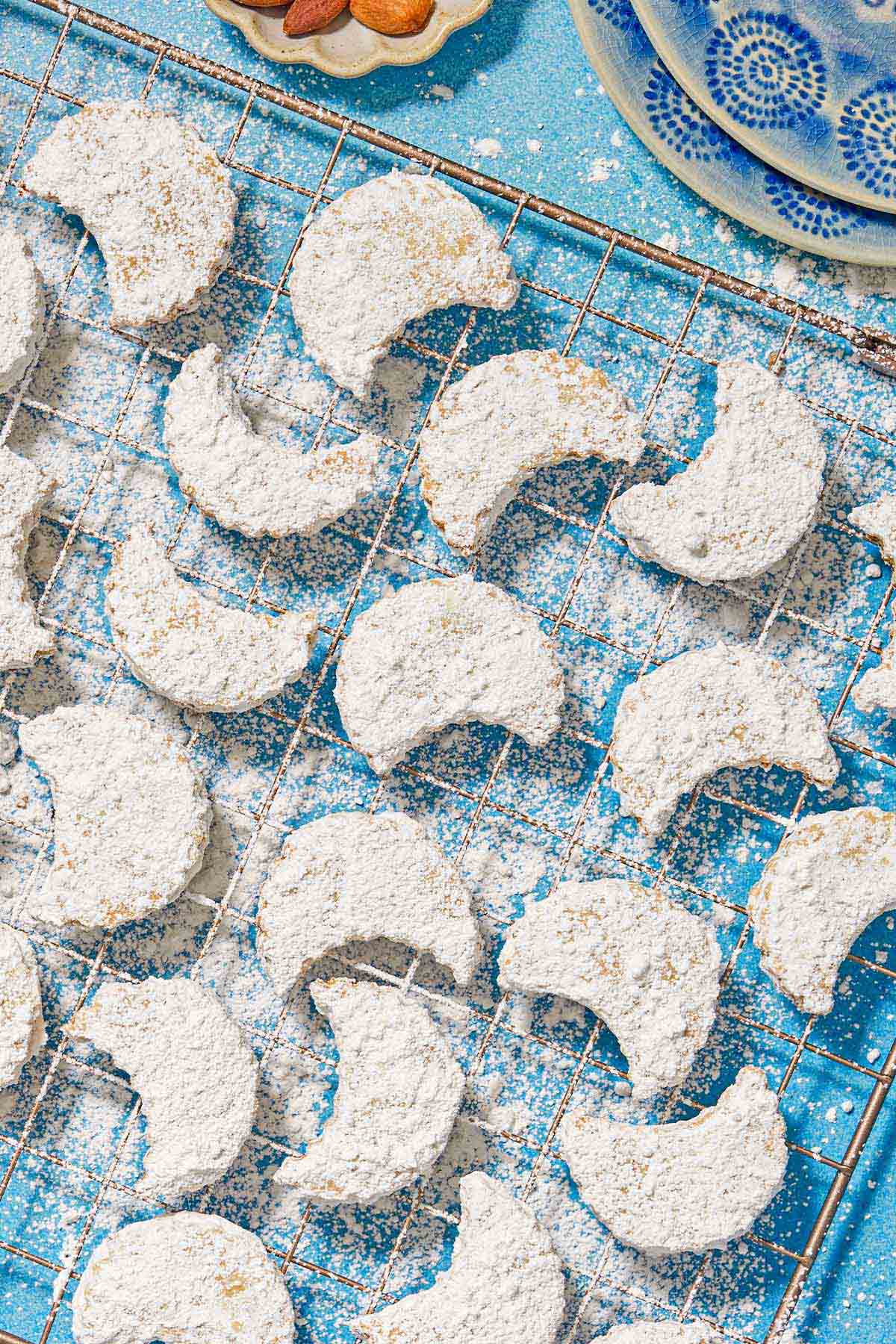 The almond cookies on a wire rack next to a stack of two plates.