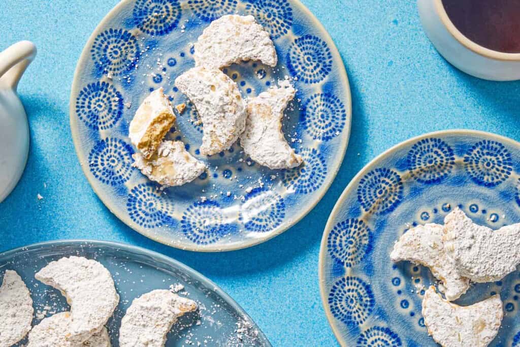 Two plates of the almond cookies next to a cup of coffee an a platter with the rest of the cookies.