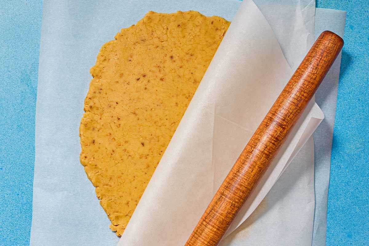 The rolled dough for the almond cookies between layers of parchment and next to a rolling pin.