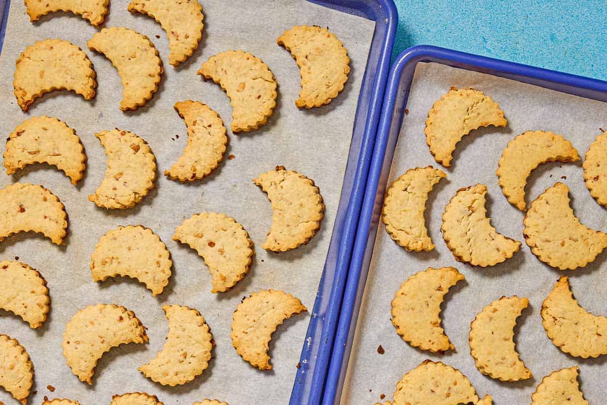 The crescent shaped baked almond cookies on 2 parchment lined sheet pans.