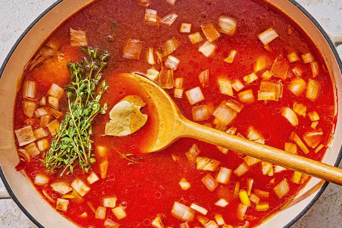 The tomato broth, vegetables, seasonings and herbs for the bouillabaisse in a pot with a wooden spoon.