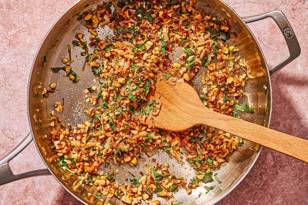 The aromatics for the butternut squash pasta being sautéed in a skillet with a wooden spoon.