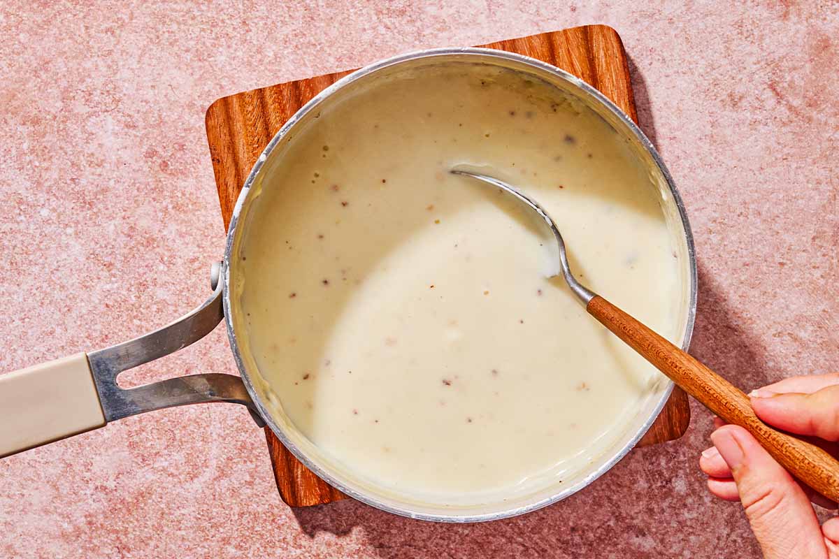 The bechamel sauce in a saucepan being stirred with a spoon.