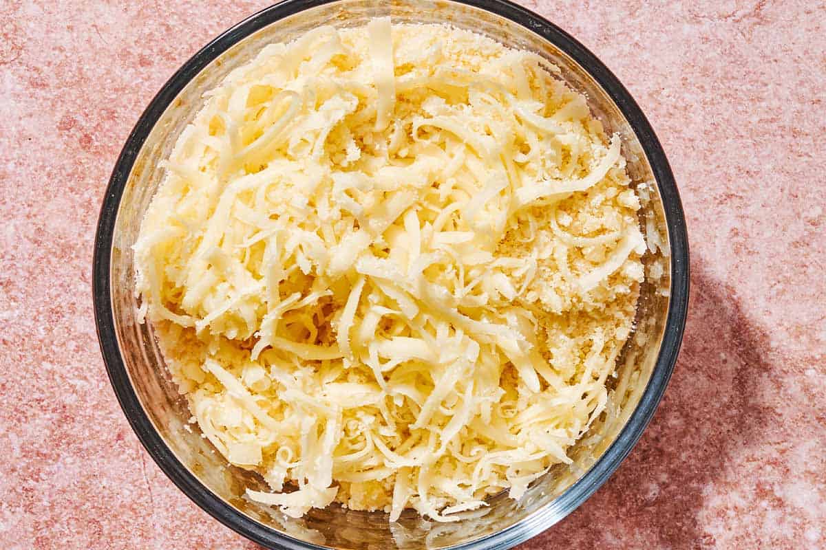 Grated Parmigiano-Reggiano cheese mixed with coarsely grated mozzarella cheese in a bowl.