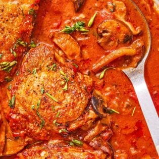 Chicken chasseur in a skillet with a serving spoon.