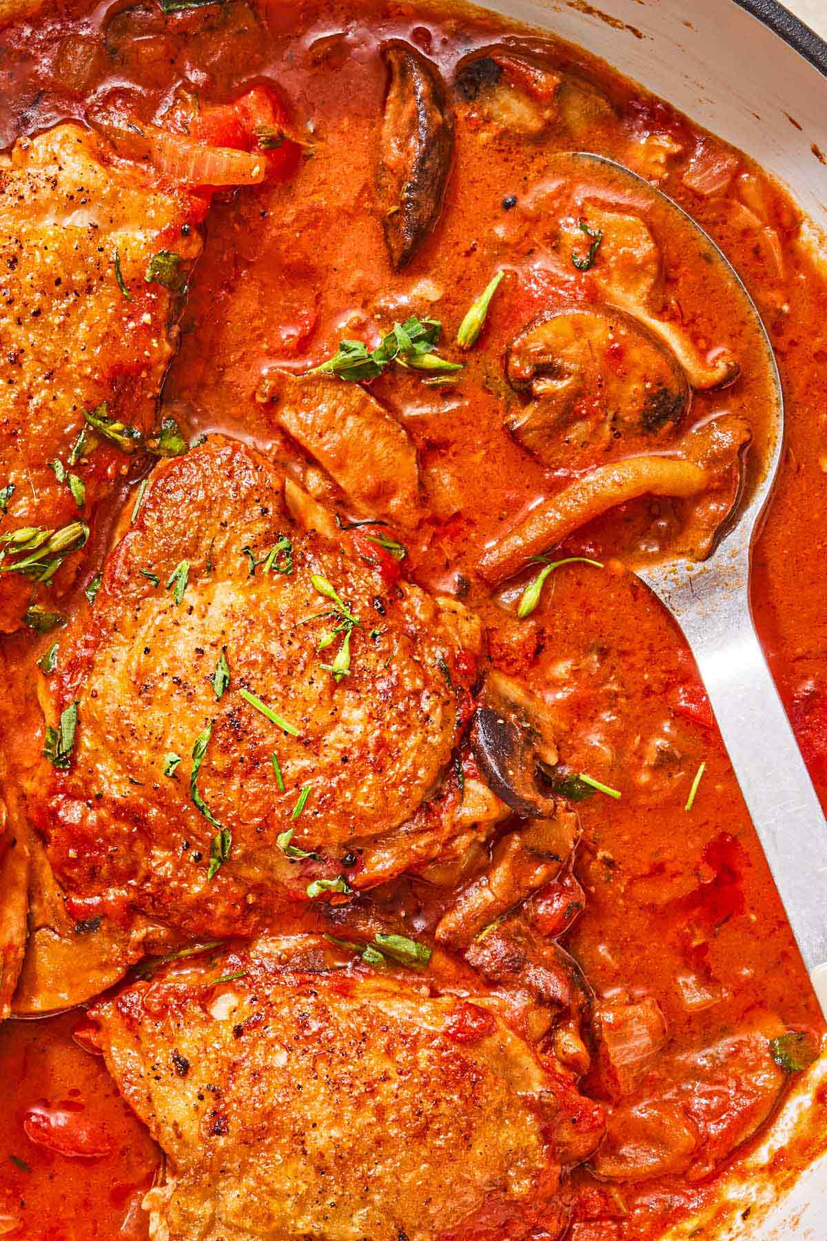 Chicken chasseur in a skillet with a serving spoon.