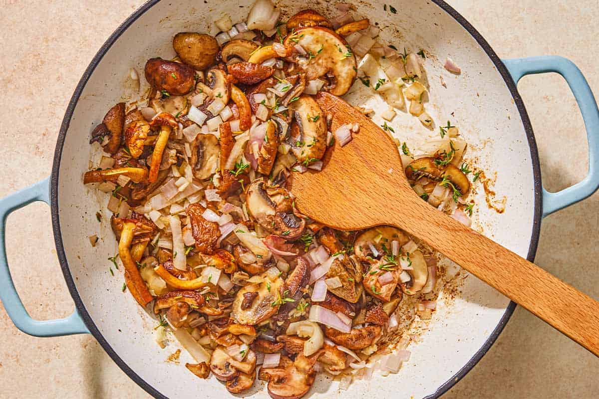 The vegetables for the chicken chasseur being sauteed in a skillet with a wooden spoon.