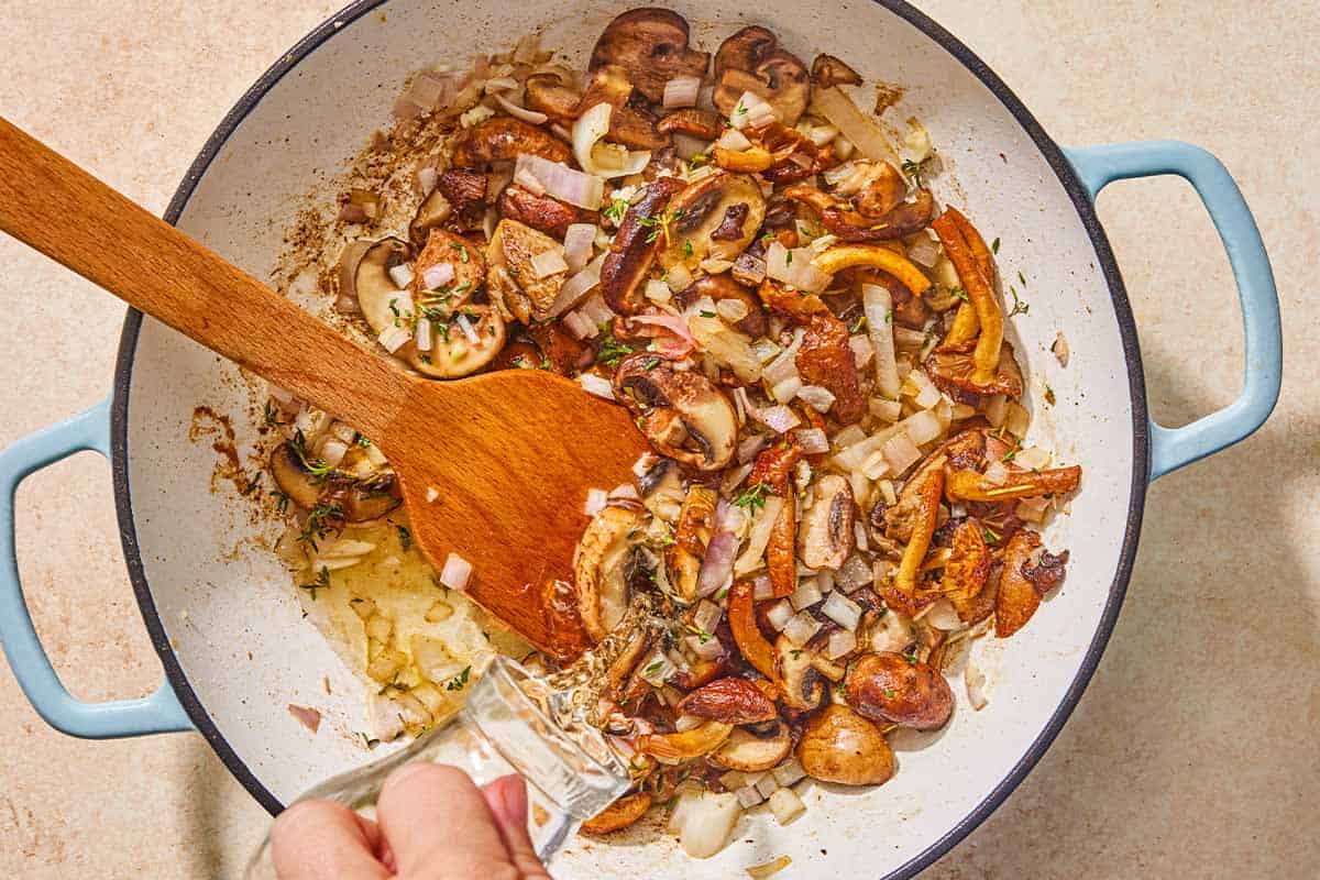 The wine being added to the sauteed vegetables in the skillet with a wooden spoon.