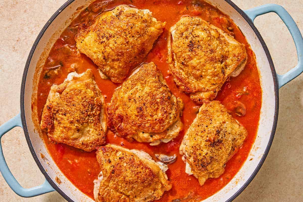 The chicken thighs for the chicken chasseur simmering with the vegetables and tomato sauce in the skillet.