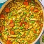 Chicken orzo soup in a pot. Next to this is a bowl of chopped green onions and 2 juiced lemon halves.