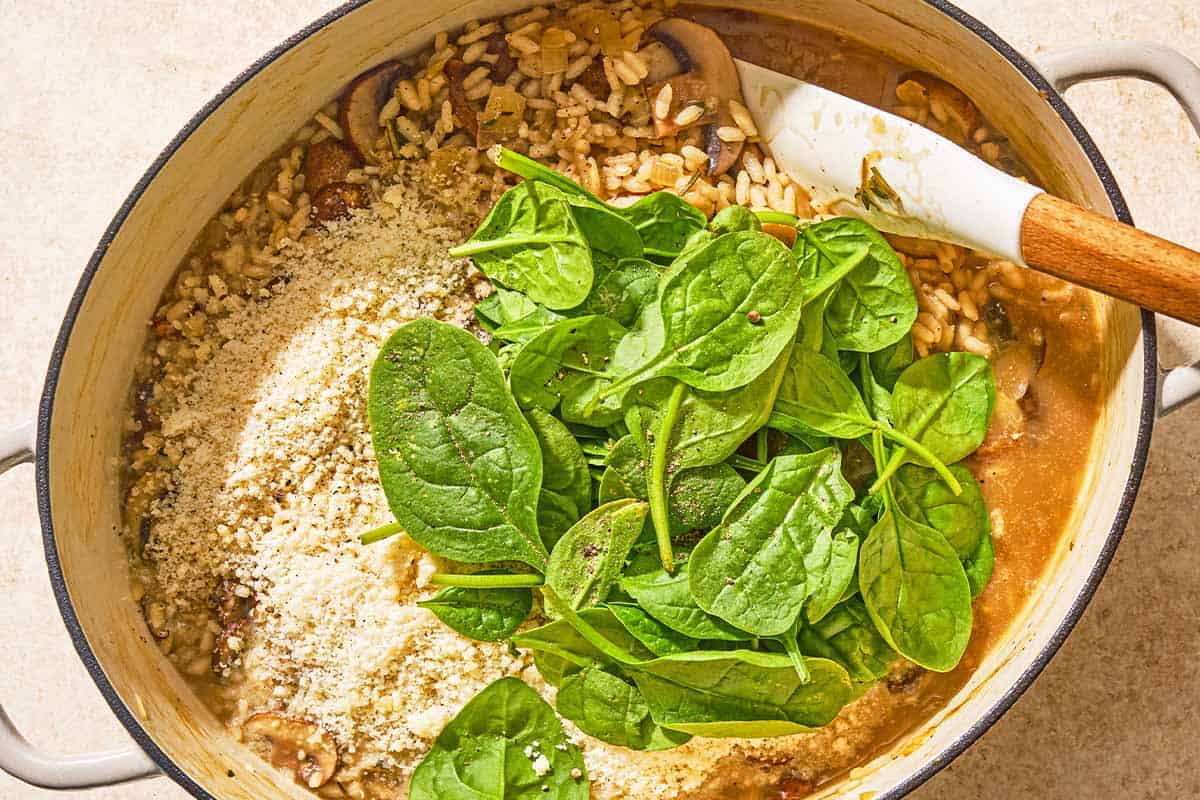 The spinach and cheese being stirred into the chicken risotto in a large pot with a spatula.