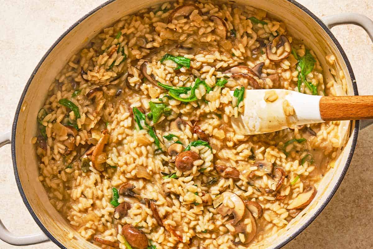 The spinach and cheese being stirred into the chicken risotto in a large pot with a spatula.