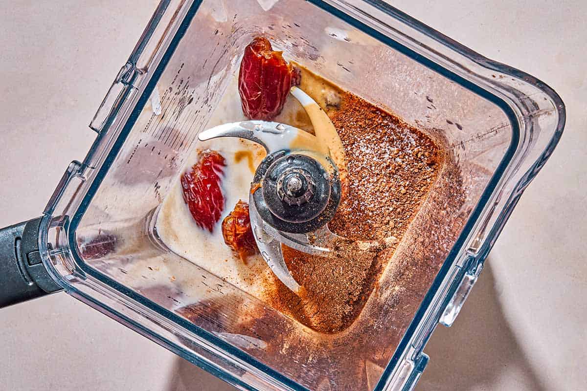 The ingredients for the vegan eggnog in the pitcher of a blender just before being mixed together.