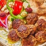 A serving of greek meatballs on a plate with pita, tzatziki sauce and a Greek salad.
