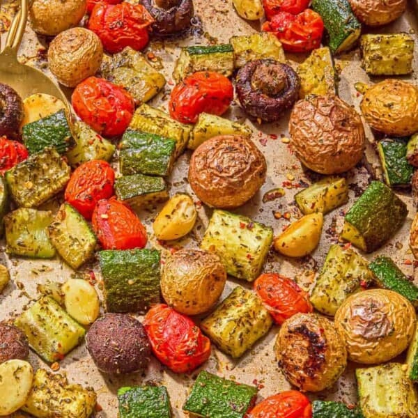 The roasted vegetables recipe on a sheet pan with serving utensils.