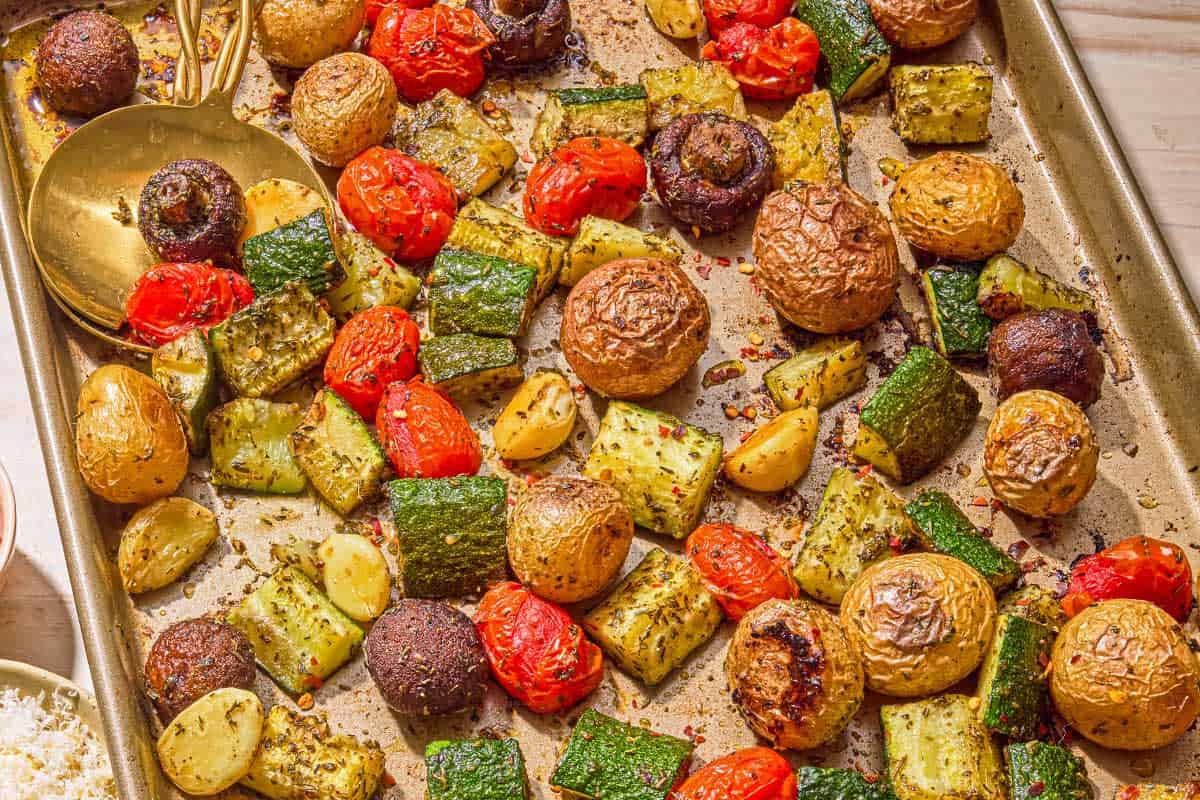 The roasted vegetables recipe on a sheet pan with serving utensils.